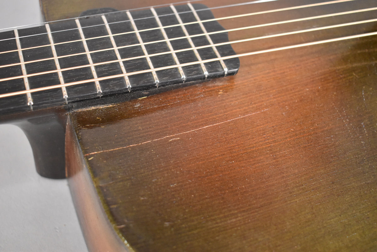 Close-up of the guitar's dark brown body and black fretboard, showing finish wear, scratches, and a long crack on the body.