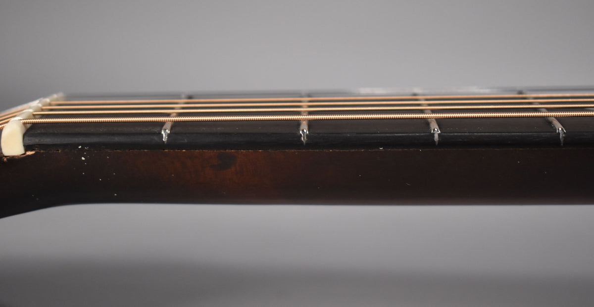 Close-up of the dark brown fretboard and neck from the side, showing the nut, six strings, and some white wear on the neck.