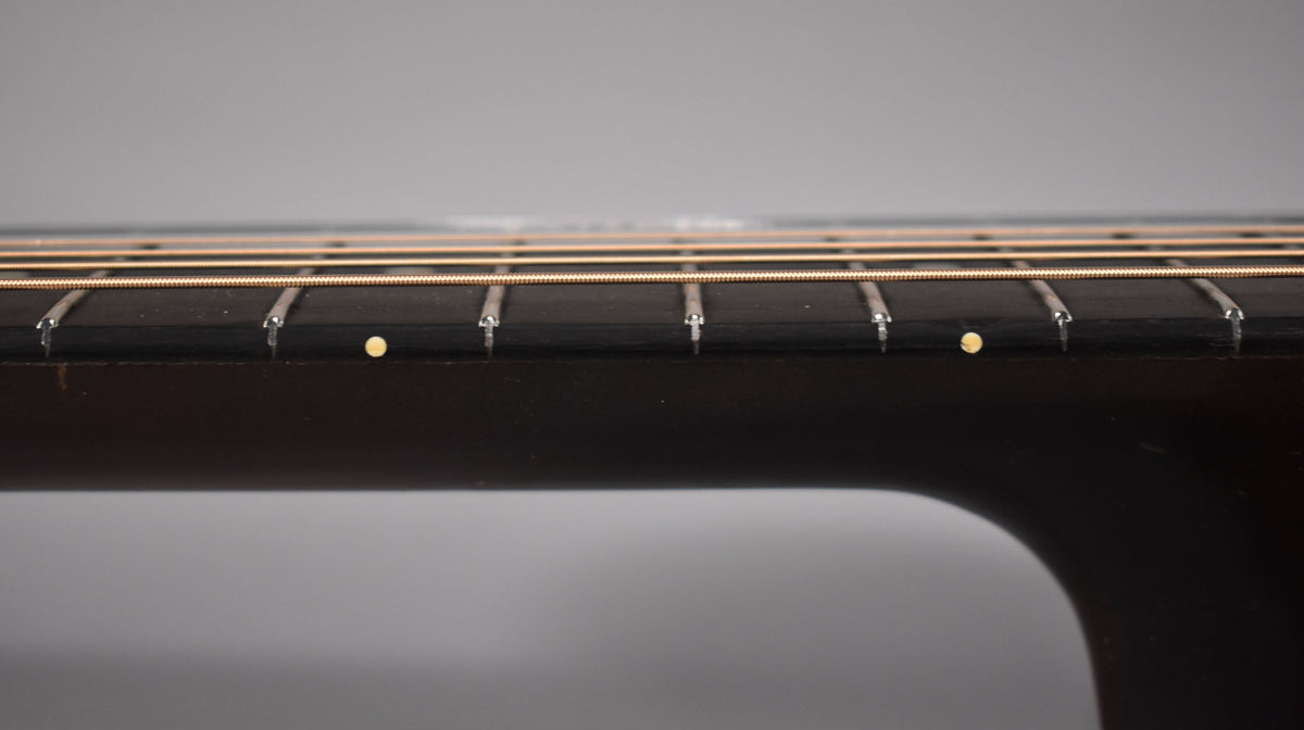 Close-up of the dark fretboard and neck, showing five frets, six strings, and two small, round, light-colored fret markers.