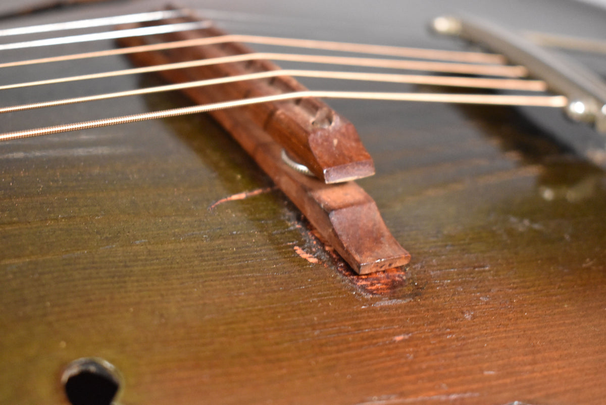 Close-up of the guitar's dark sunburst top, showing the two-piece wooden bridge with significant finish wear and exposed wood around its base.