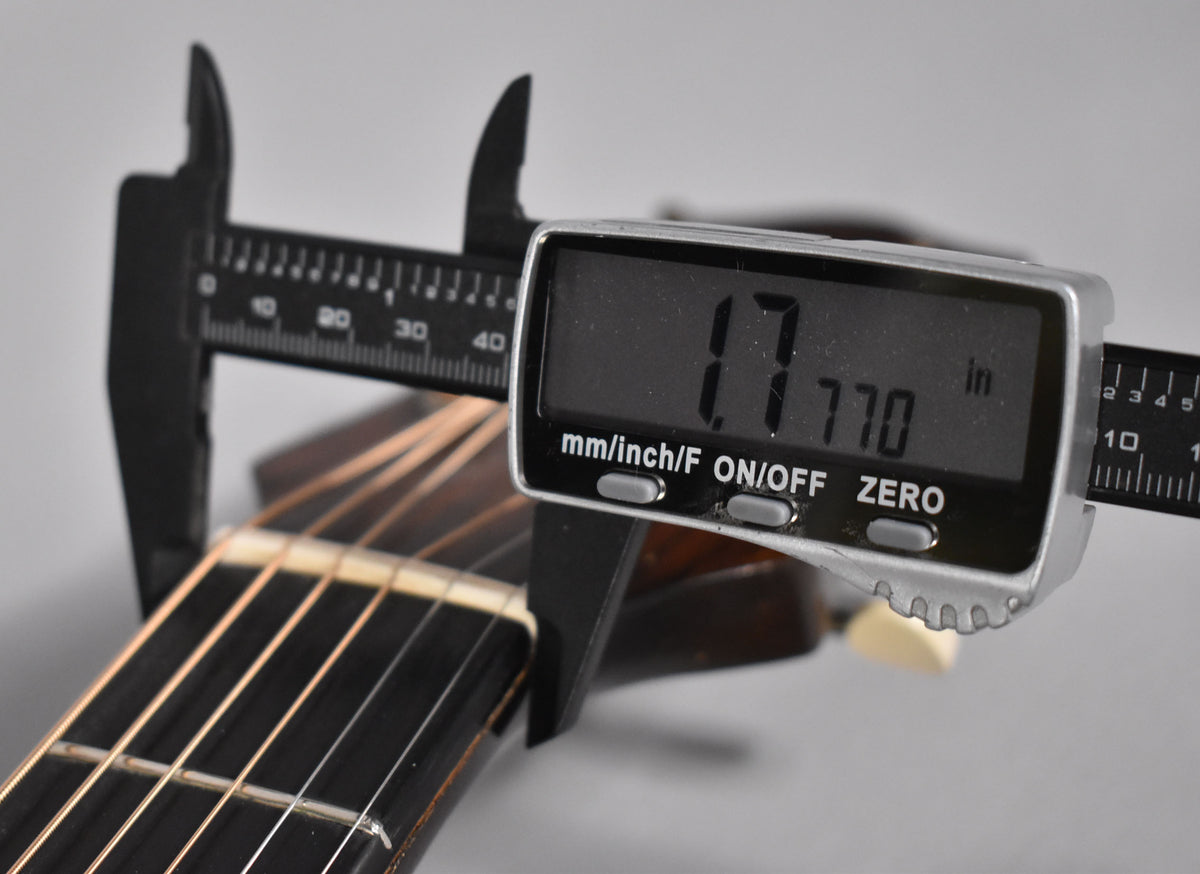 A digital caliper measures the guitar's nut width at 1.770 inches, clamped over the dark fretboard and light nut.