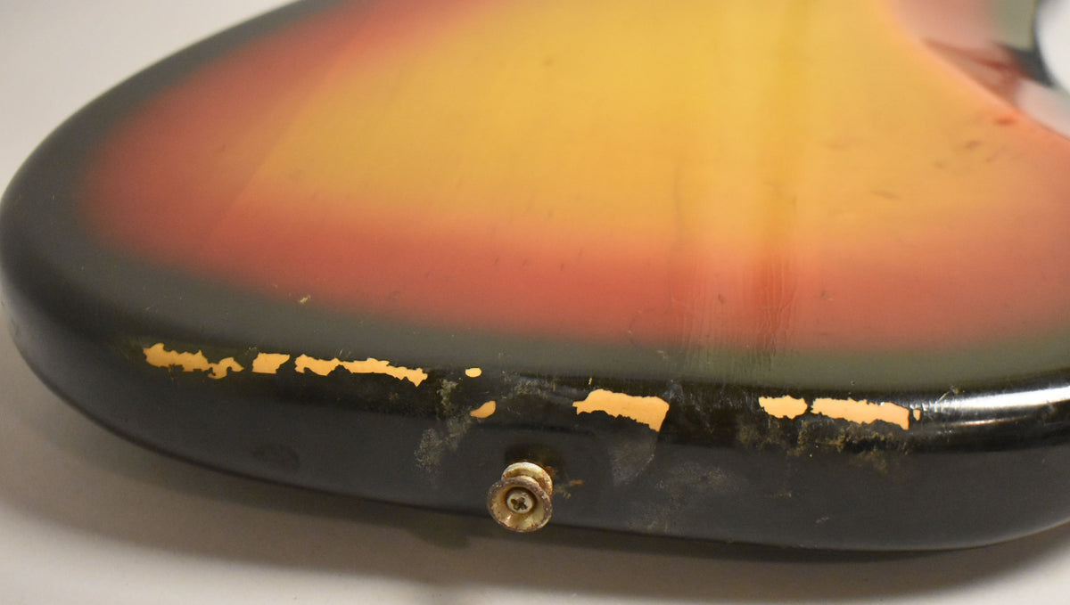 Close-up of the bass body's lower bout, showing the sunburst finish with significant paint chipping and a worn output jack.
