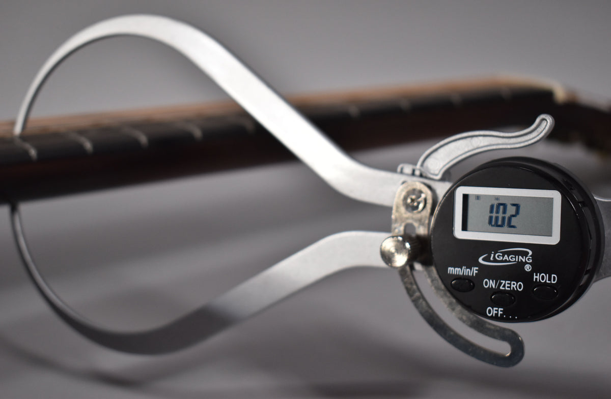 A digital caliper measures the neck thickness at the first fret, showing "1.02" on its screen.