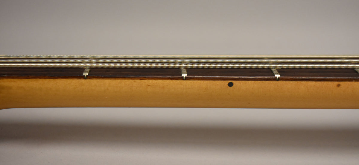 Close-up of the bass neck from the side, showing the dark fretboard, light maple neck, and a small black dot inlay.