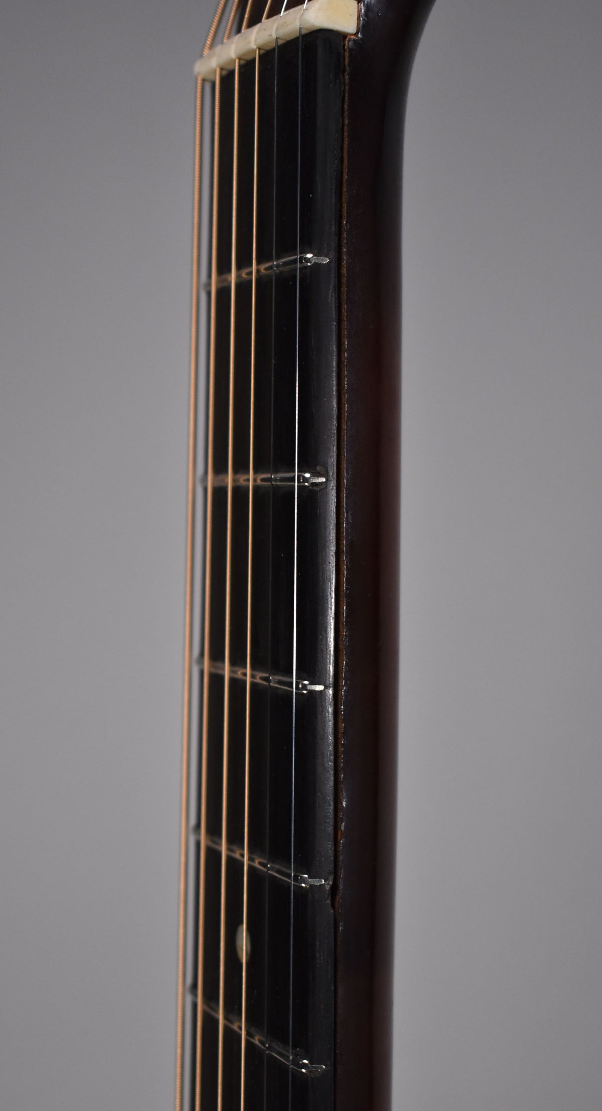 Close-up of the guitar's dark brown neck and fretboard, showing light strings, frets, and a small dot inlay on the 7th fret.