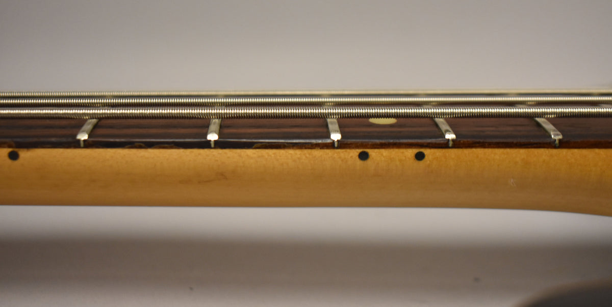 Close-up of the bass neck and fretboard, showing four strings, dark wood, light maple, and small black dot inlays.