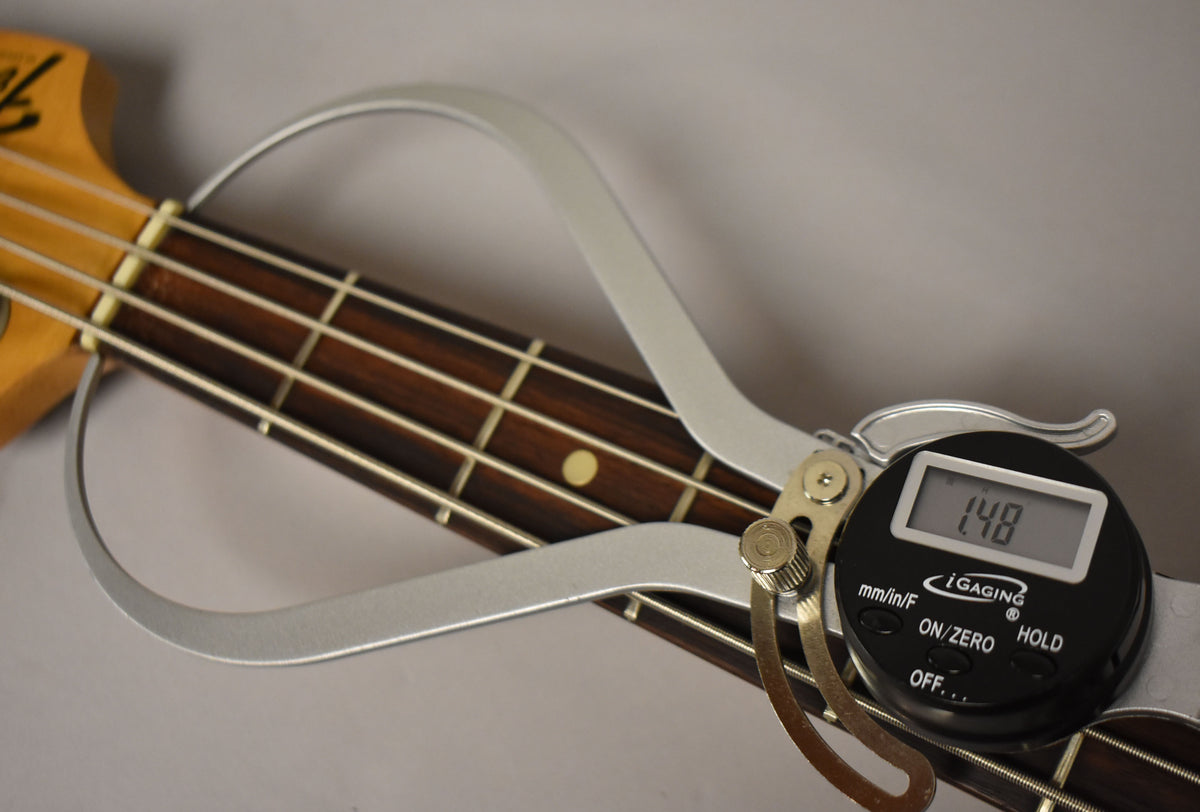 A close-up of the bass neck with a digital caliper measuring the fretboard width at the nut, showing "1.48" on its display.