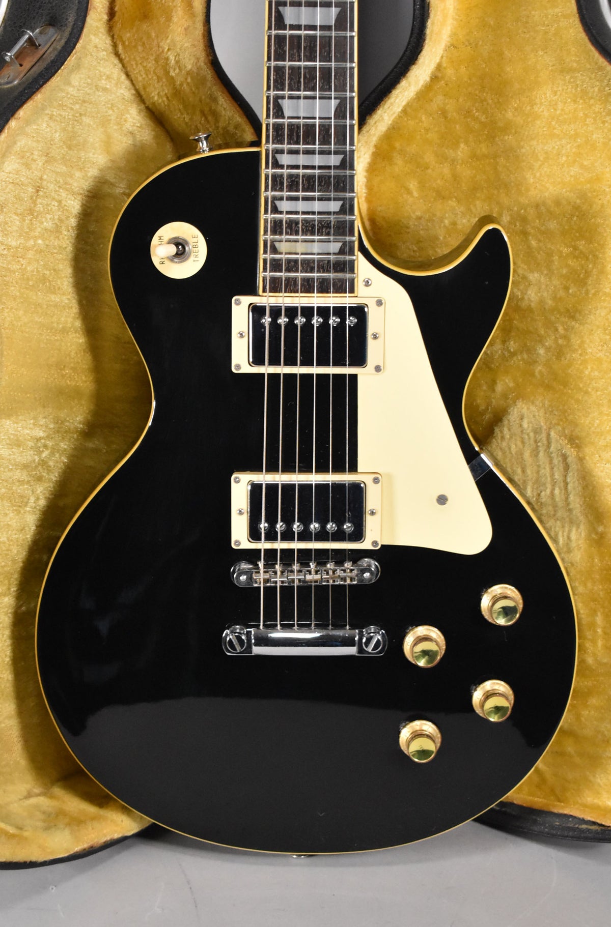 Full-frame view of a black Les Paul-style guitar with cream binding, pickguard, pickup rings, and switch tip, in a gold-lined case.