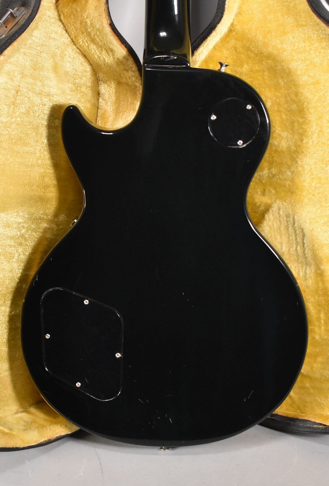 The guitar's glossy black back, with two control plates, shows light scratches and scuffs, resting in a yellow-lined hard case.