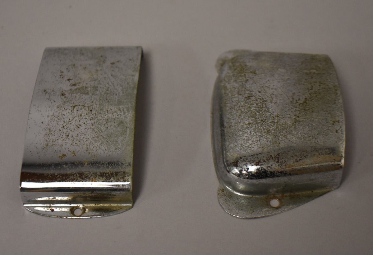 Two tarnished chrome covers, one curved and one rectangular, both with visible mounting holes and heavy pitting.