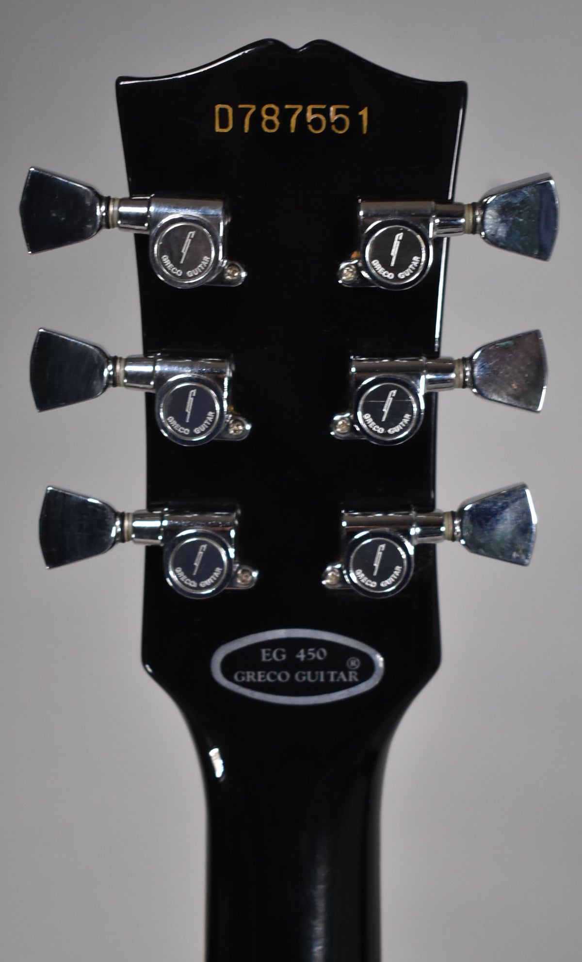 Rear view of the black gloss headstock with six chrome tuners, showing some tarnishing and light wear.