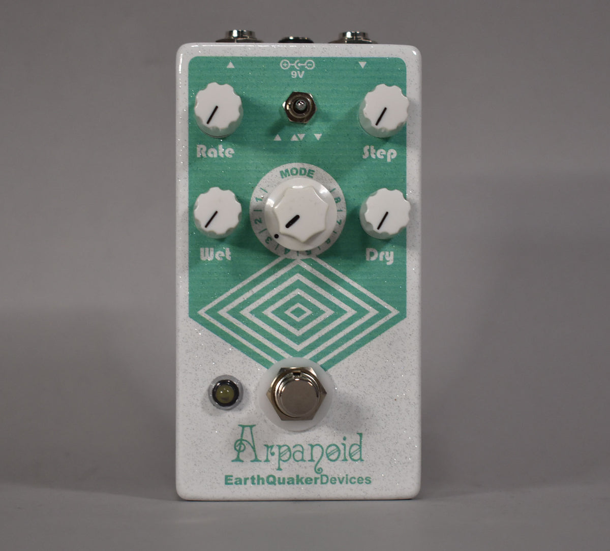A white glitter-finish pedal with a teal geometric design, five white knobs, a footswitch, and an LED.
