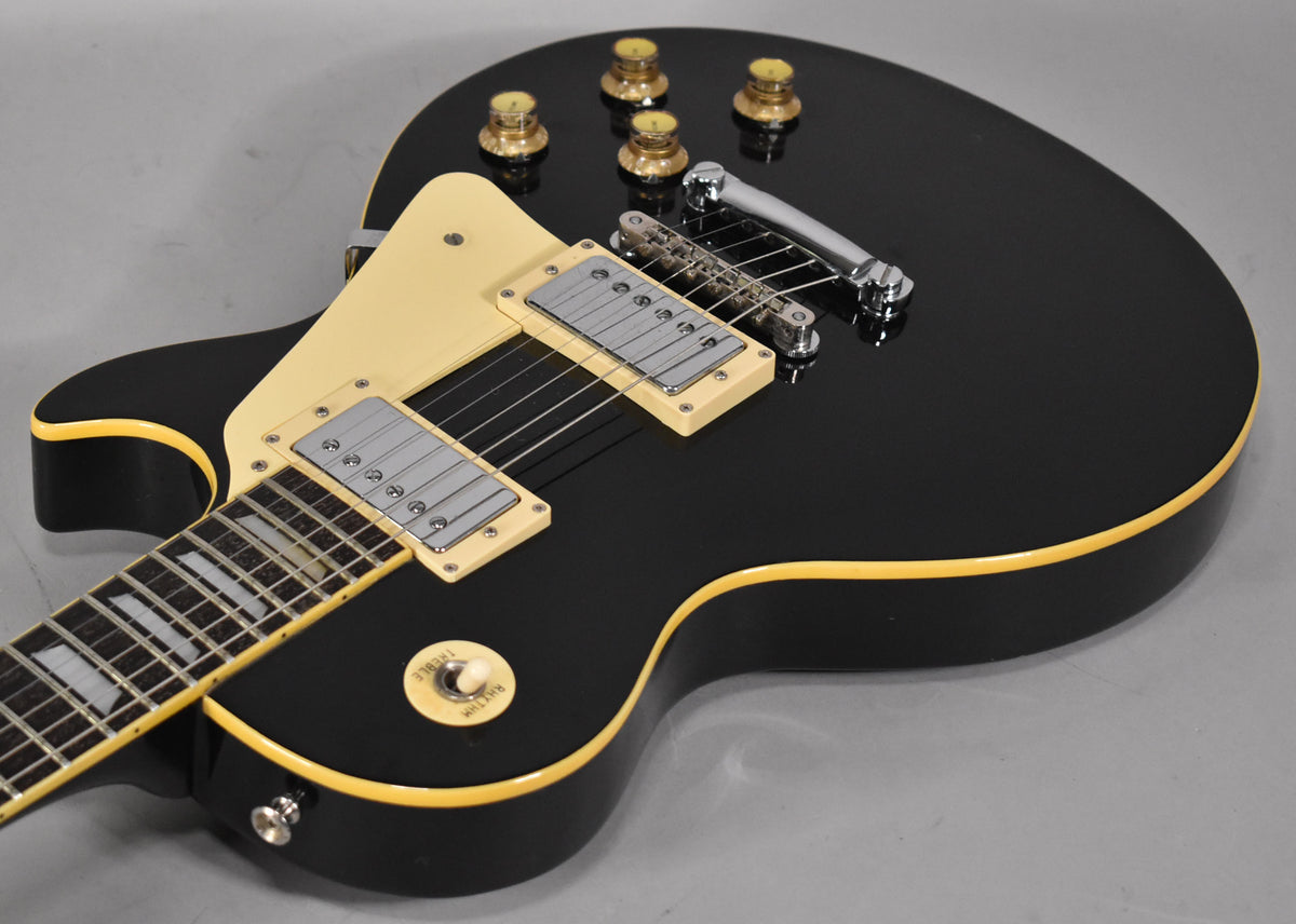 Black guitar body with cream binding, two humbuckers, a cream pickguard, four amber knobs, and a chrome bridge.