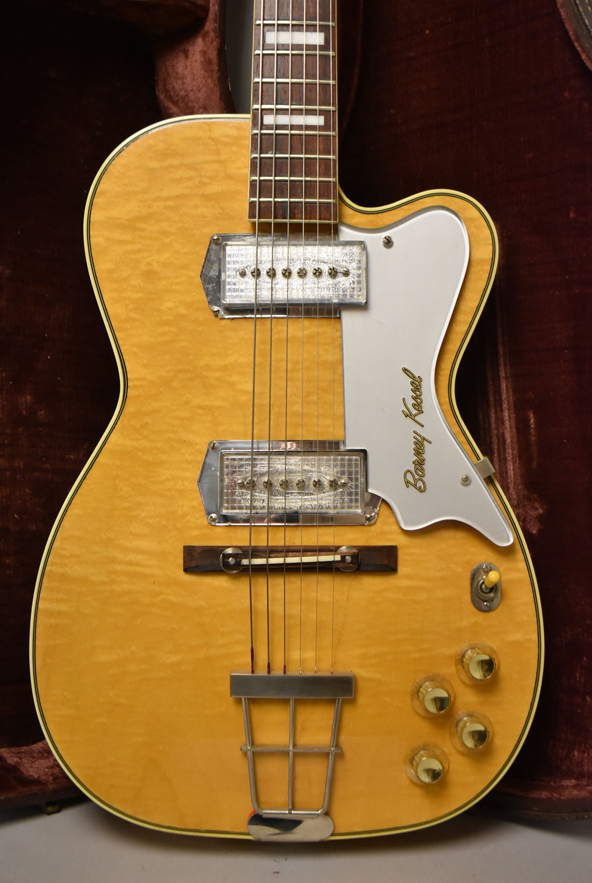 The guitar's flamed maple body, with a natural finish, shows two chrome pickups, a white pickguard, and four clear amber control knobs.