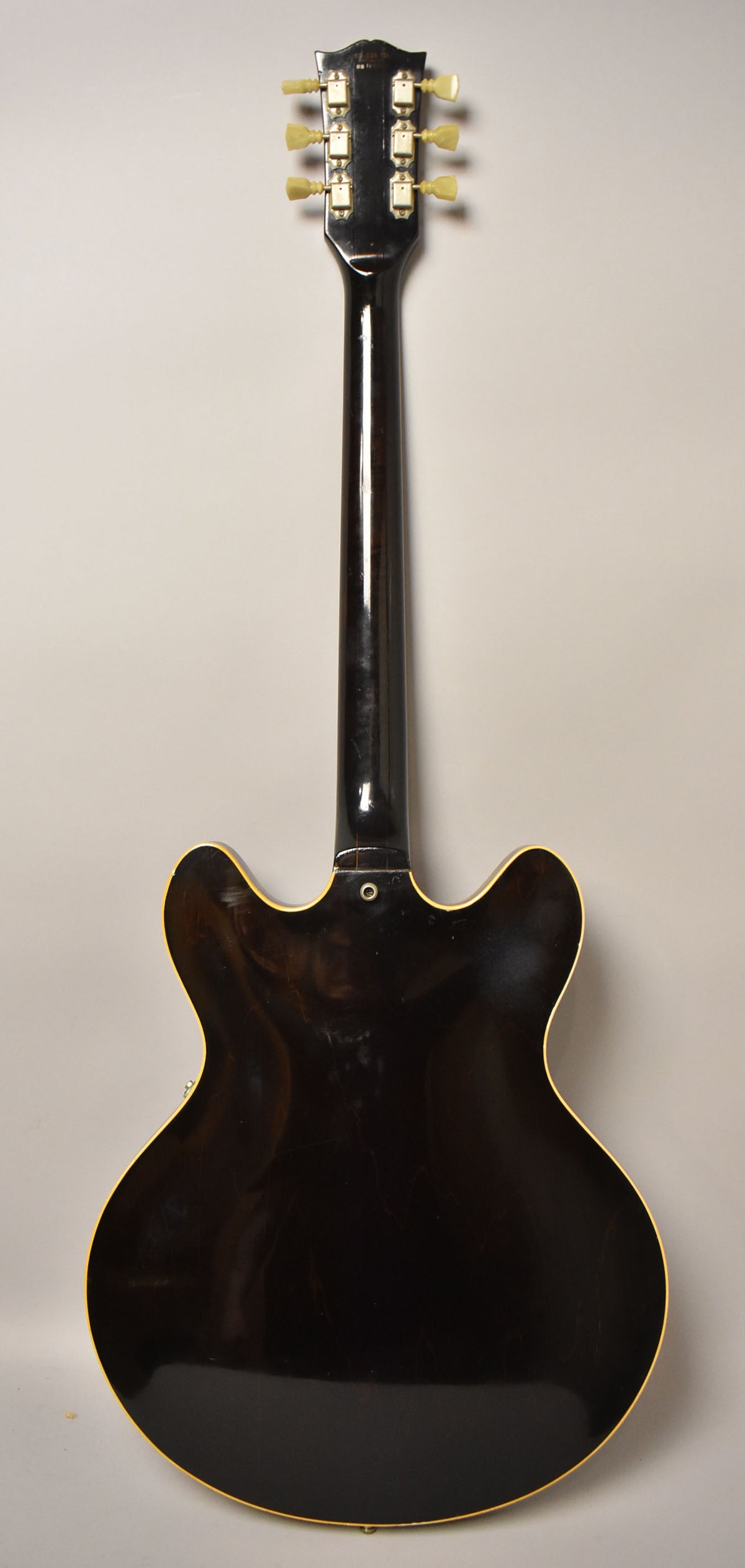 Full back view of a dark walnut semi-hollow guitar with cream binding, showing light scratches and a few dings on the body and neck.