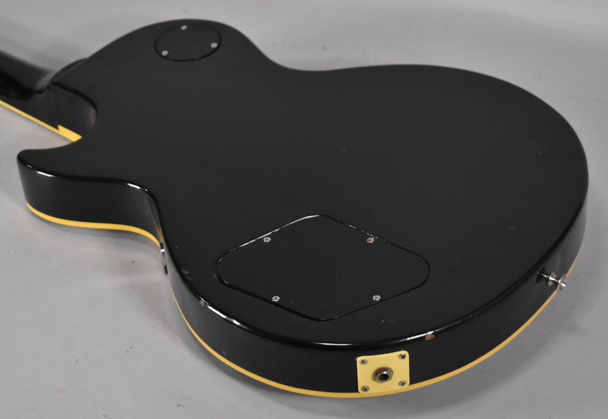 The guitar's black back with cream binding is angled, showing a control cavity cover and a cream output jack plate with wear.