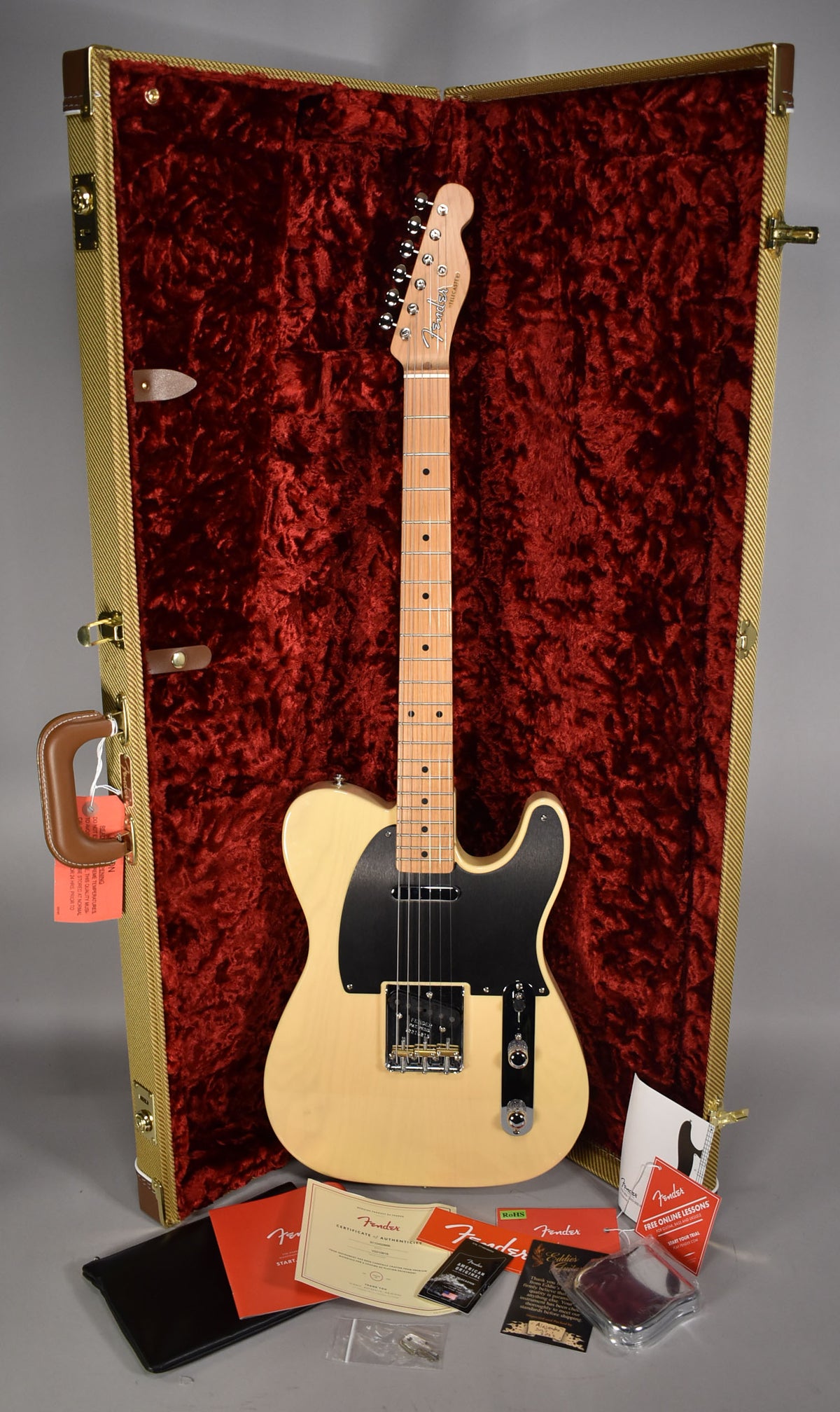Full view of a blonde Telecaster with a black pickguard, resting in its open tweed hard case with red plush lining.