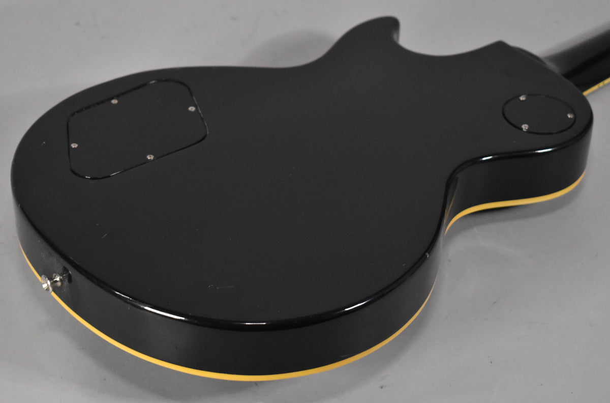 The back of a black electric guitar with cream binding, showing control cavity covers and a chrome strap button.