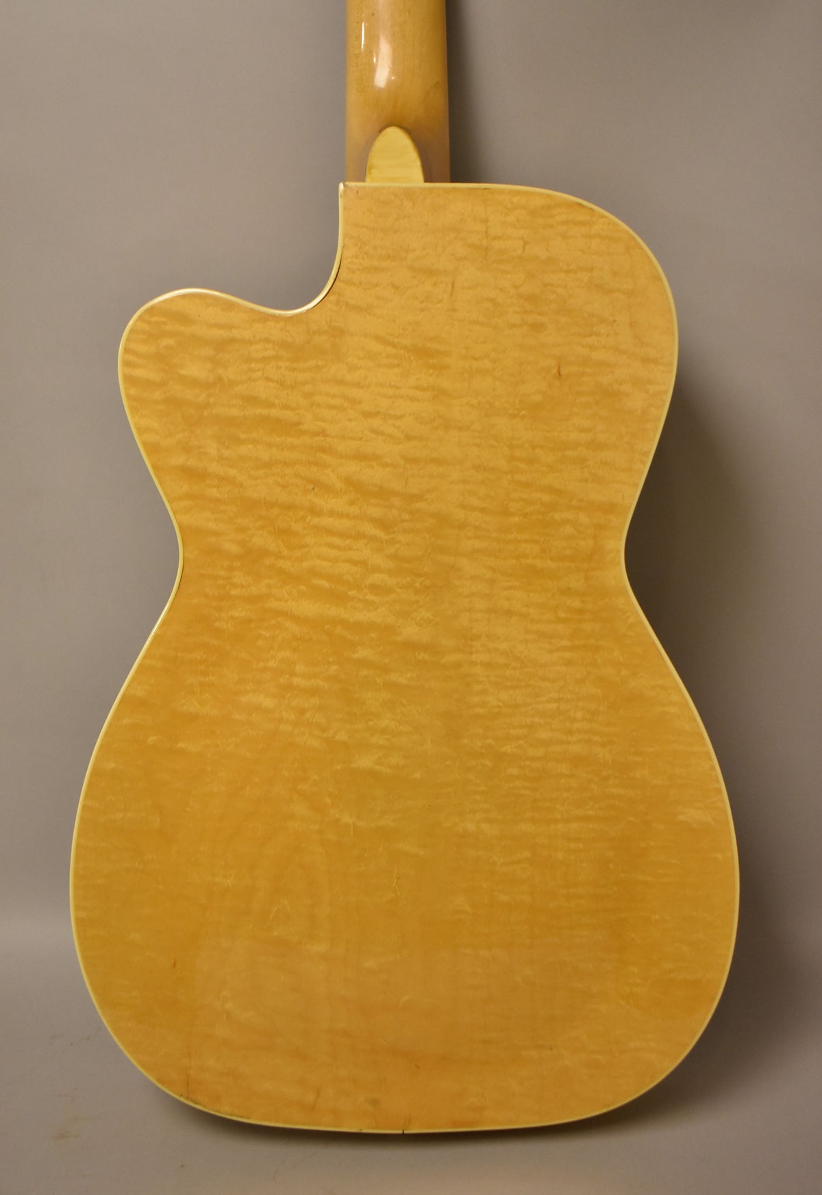 The back of a natural finish, flame maple archtop guitar with a single cutaway and a few small dings.