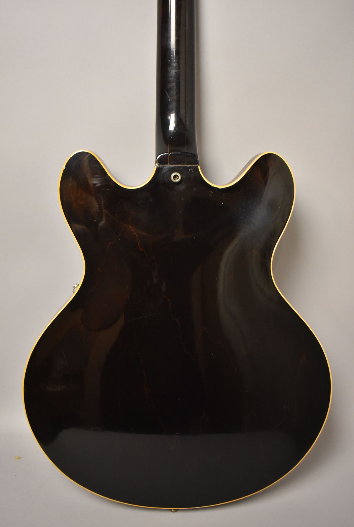 The guitar's dark walnut back shows extensive finish checking and scratches, with a strap button at the neck heel.
