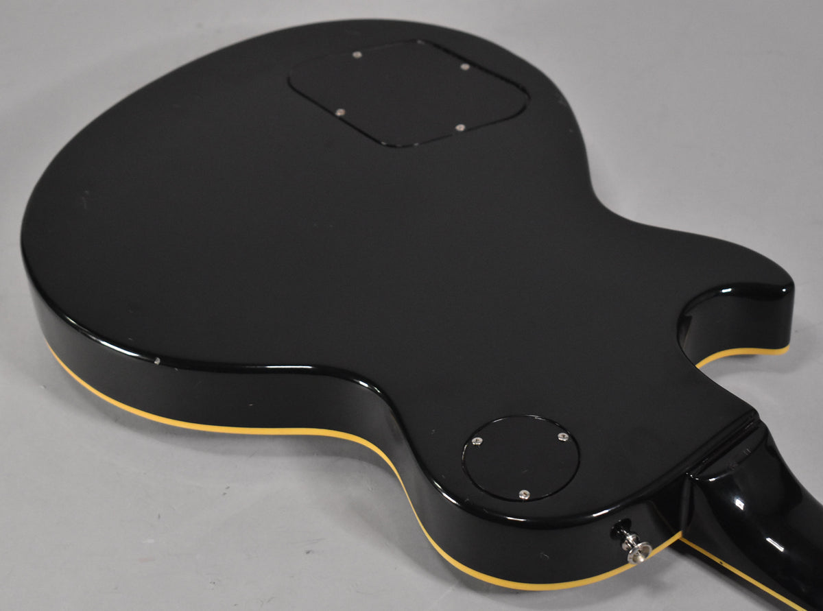 The guitar's black body, with cream binding, is shown from the back, revealing two control cavity covers and a strap button.