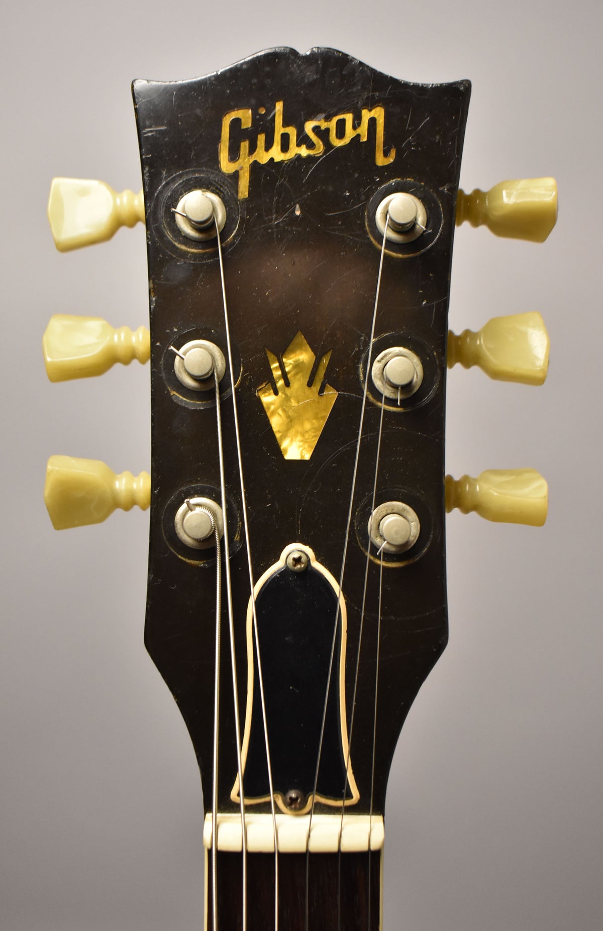 Close-up of the guitar's black headstock, showing gold lettering, a mother-of-pearl inlay, and six cream-colored tuning pegs.