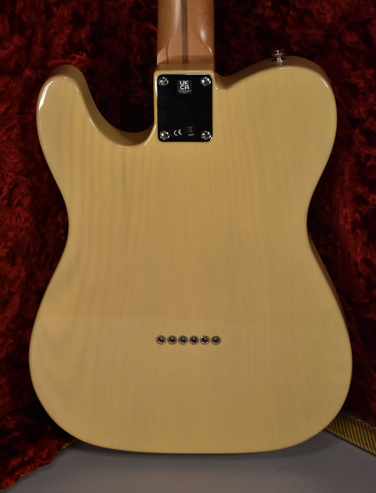 The guitar's blonde body is seen from the back, showing the neck plate, strap button, and six string-through-body ferrules.