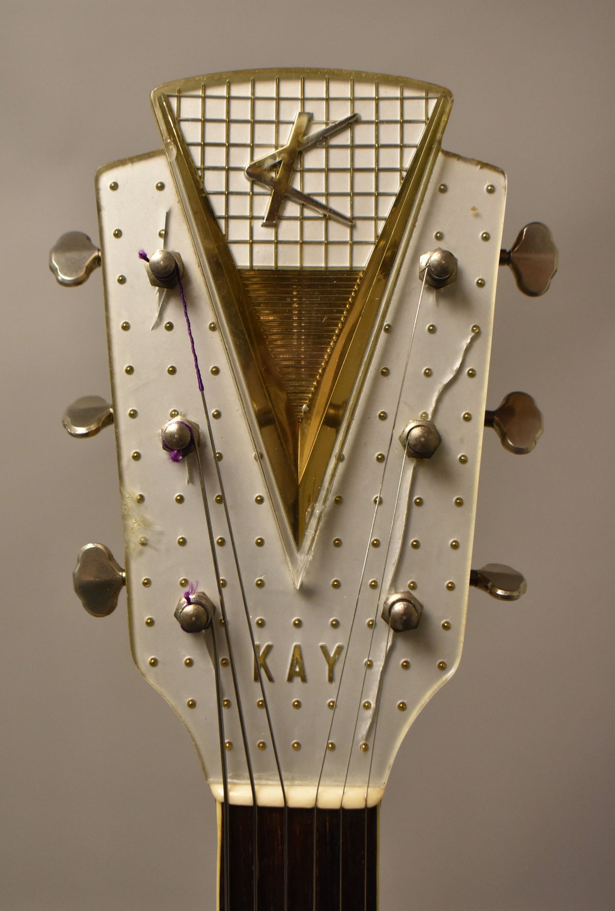 Close-up of the headstock, showing a clear plastic overlay with gold studs, a gold "K" logo, and six silver tuners.