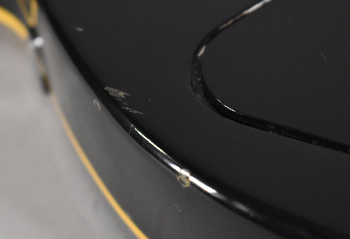 Close-up of the guitar's black body binding, showing a chip and several scratches on the upper bout, with yellow binding visible on the side.