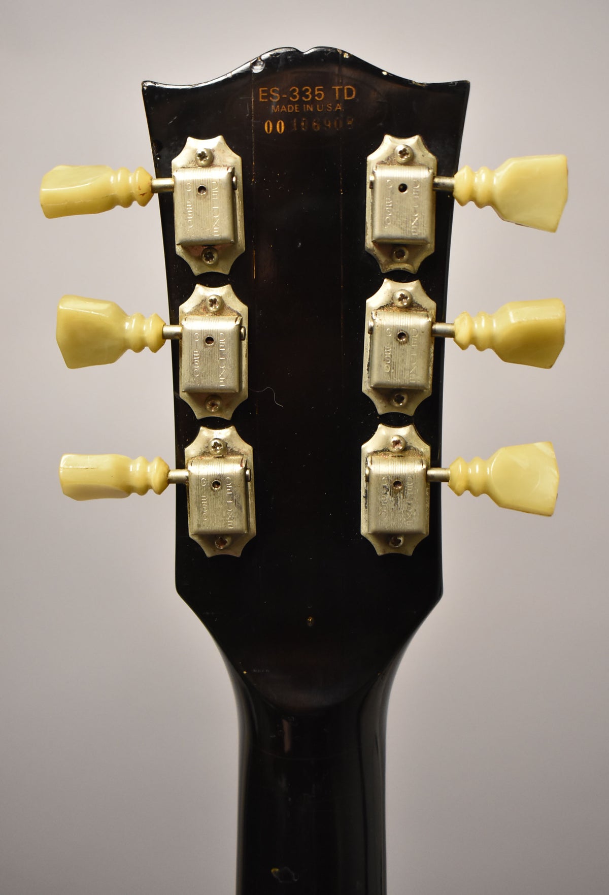 Rear view of the guitar's headstock, showing six cream-colored tuning pegs with tarnished metal housings on a dark, glossy finish.