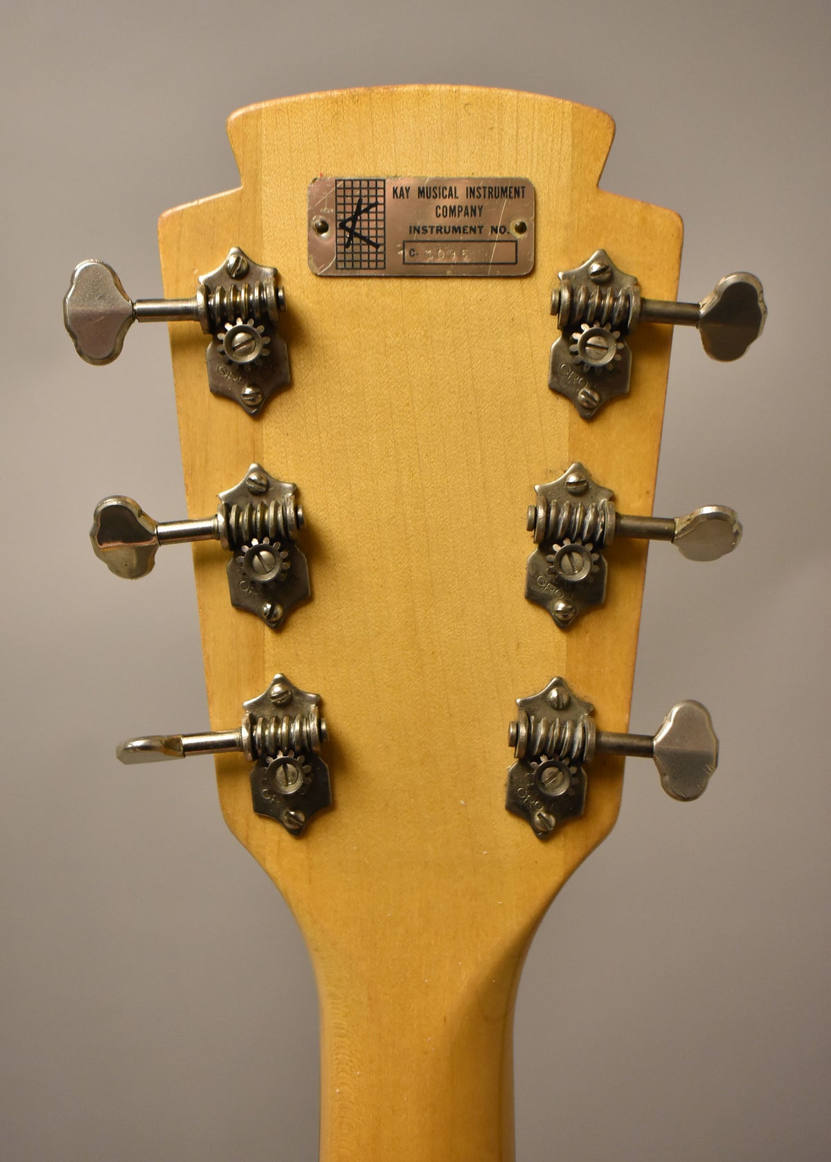 The back of the natural finish headstock shows six open-gear tuners with metal buttons and a rectangular metal serial number plate.