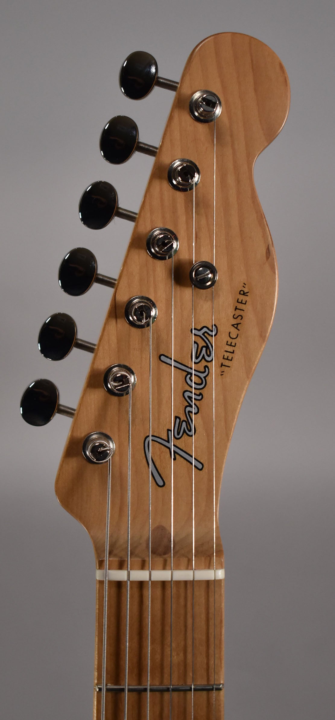 Close-up of the guitar's light brown headstock with six black tuners, silver string trees, and a white nut.