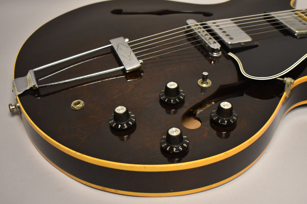 Close-up of the guitar's lower body, showing the dark walnut finish, four black control knobs, chrome trapeze tailpiece, and binding.