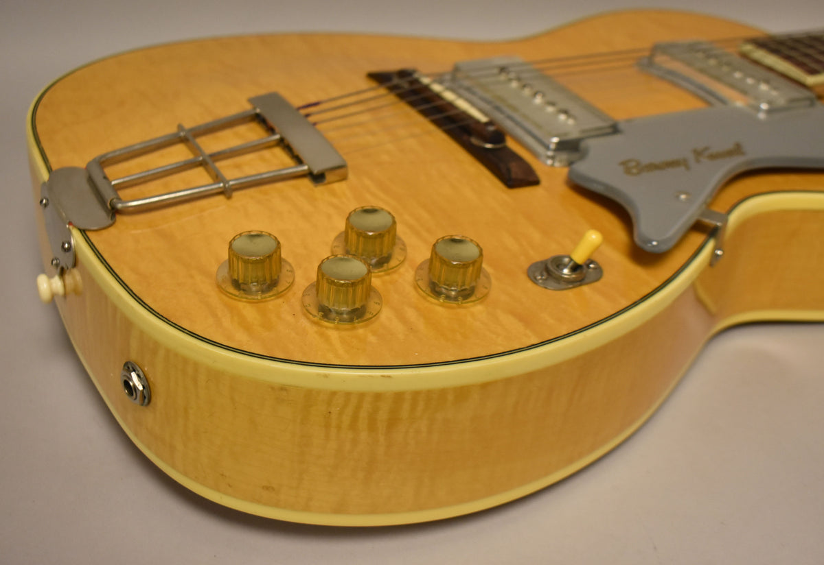 Close-up of the natural finish body, showing four amber knobs, a yellow switch tip, and a chrome trapeze tailpiece.