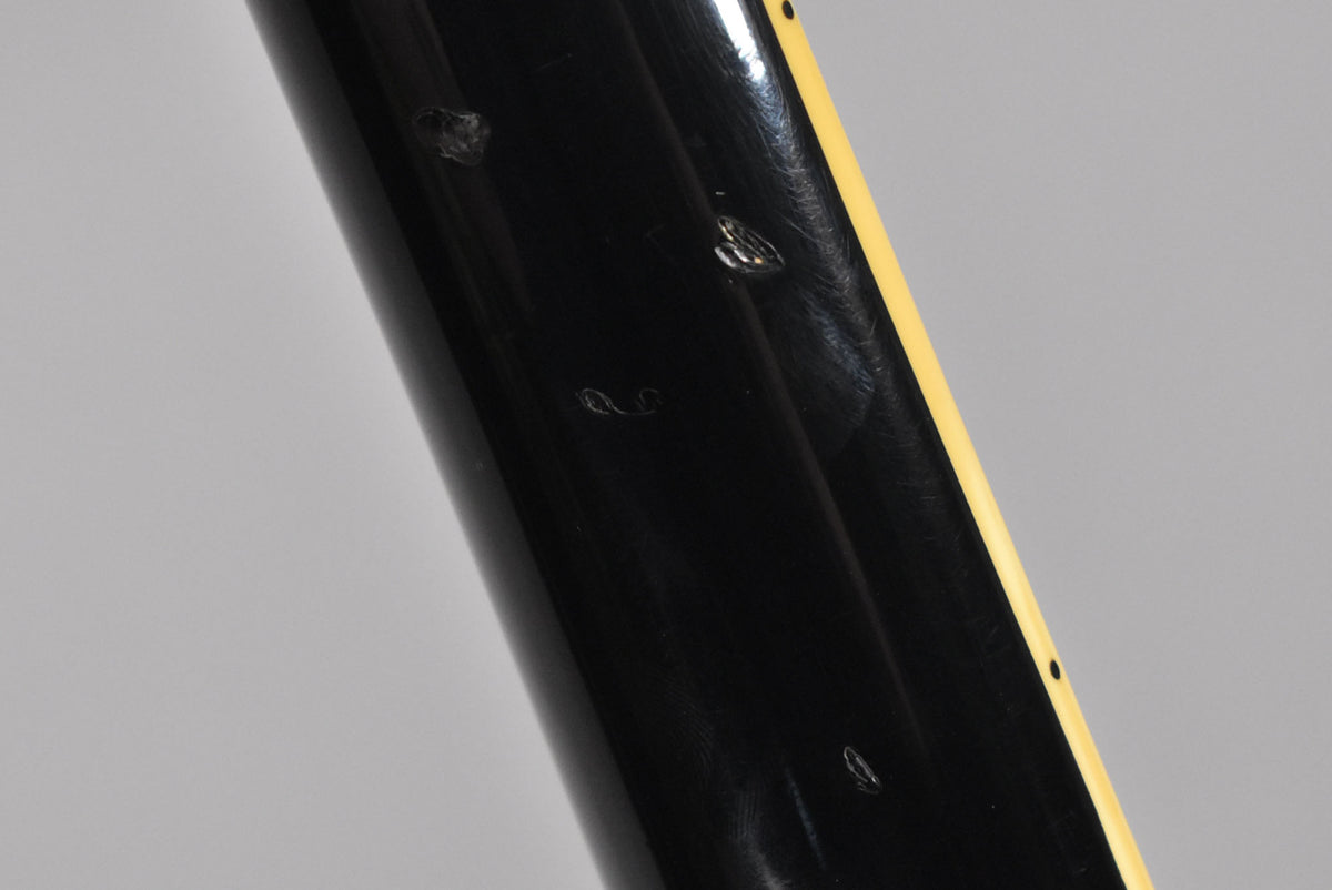 Close-up of the black gloss finish on the guitar's neck, showing several chips and dents, with cream binding visible on the right.