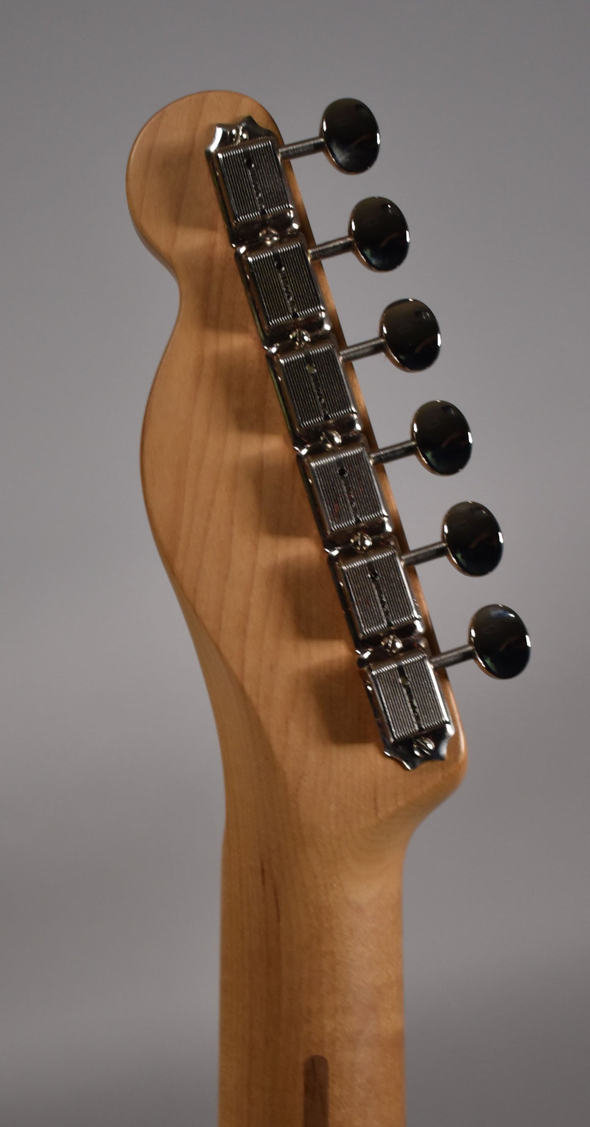 The guitar's light blonde headstock and neck are angled, showing six chrome tuners with oval buttons and ribbed casings.