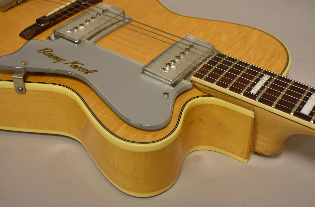 Close-up of the natural finish archtop body, showing the grey pickguard, two clear pickup covers, and the lower fretboard.