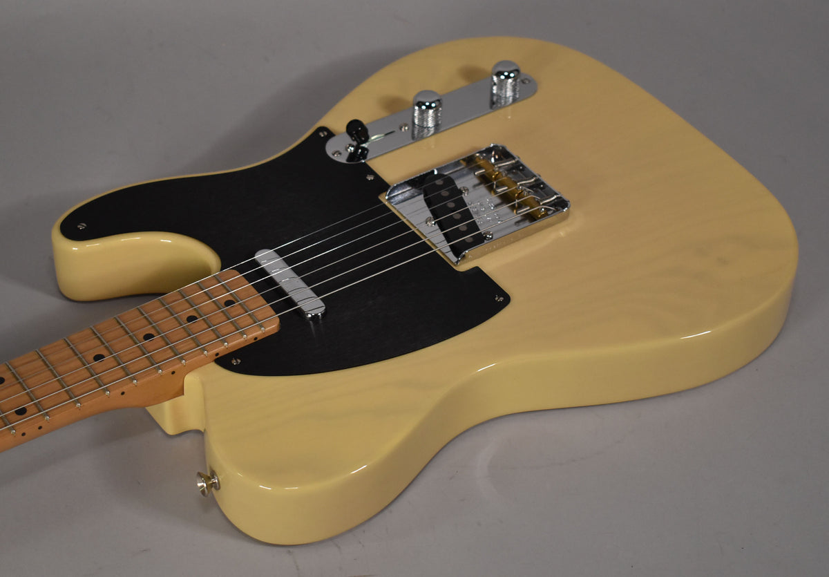 Cream-colored electric guitar, angled from the lower bout, showing a black pickguard, chrome bridge, and control plate.