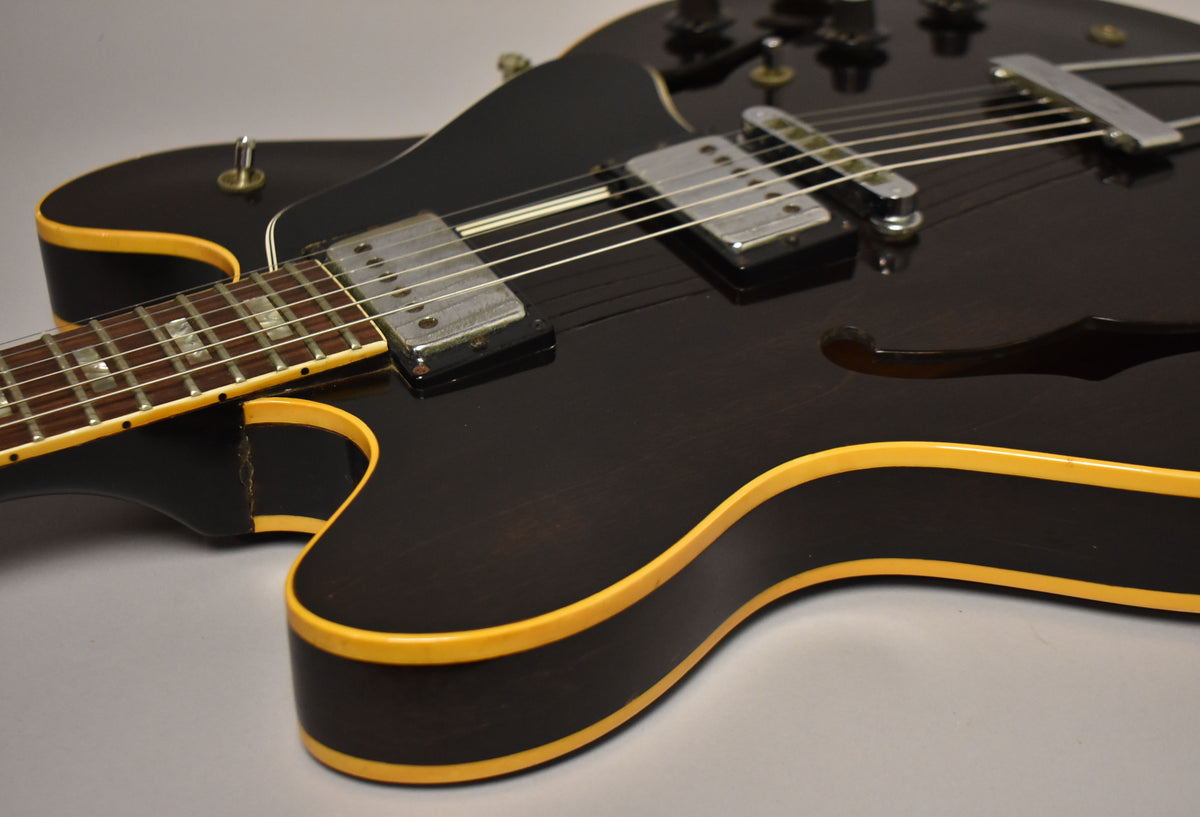 Close-up of a dark walnut semi-hollow guitar with cream binding, showing the neck joint, body, and two humbucker pickups.