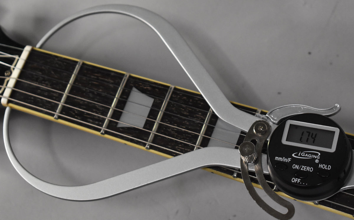 Close-up of the guitar's dark fretboard with trapezoid inlays, showing a digital fret rocker measuring fret height.