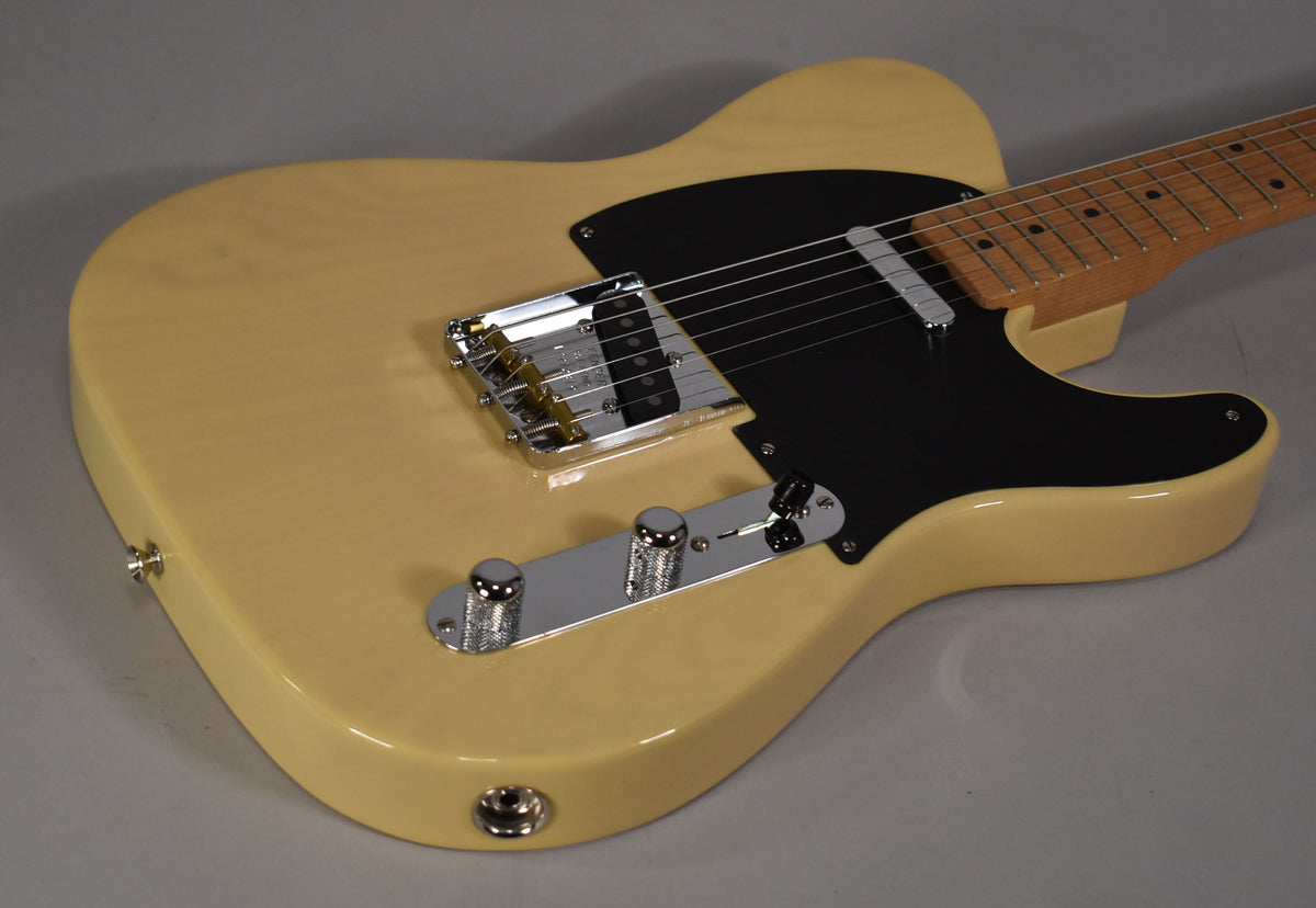 The blonde Telecaster body is angled from the lower left, showing its black pickguard, chrome bridge, control plate, and maple fretboard.