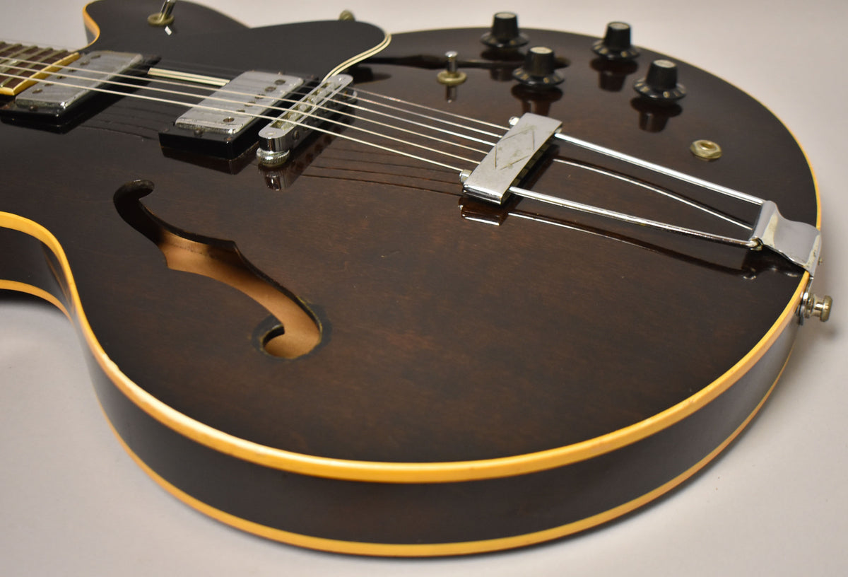 Close-up of a dark walnut hollow-body electric guitar, showing the lower bout, f-hole, chrome trapeze tailpiece, and four black control knobs.