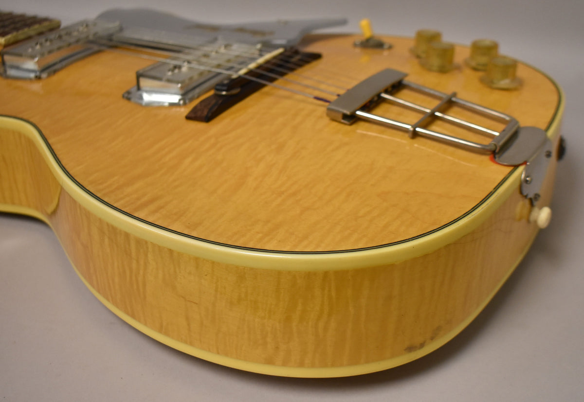Close-up of the natural finish, flamed maple body, showing the trapeze tailpiece, four amber control knobs, and some wear on the lower bout.