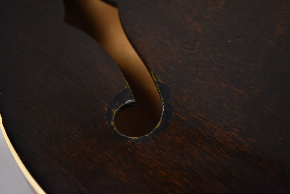 Close-up of the lower f-hole on the dark walnut body, showing wear and chipping around the edges and light binding.