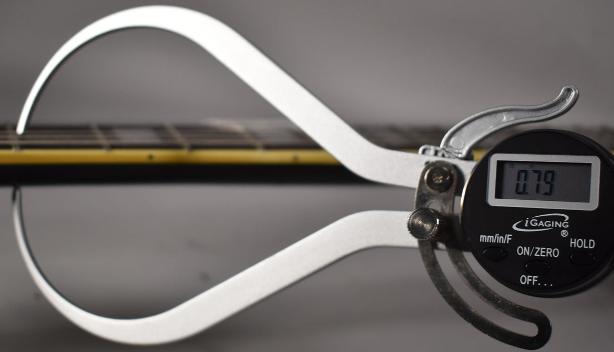 A digital caliper measures the guitar's neck thickness at 0.79 inches, showing the fretboard and strings from a side view.