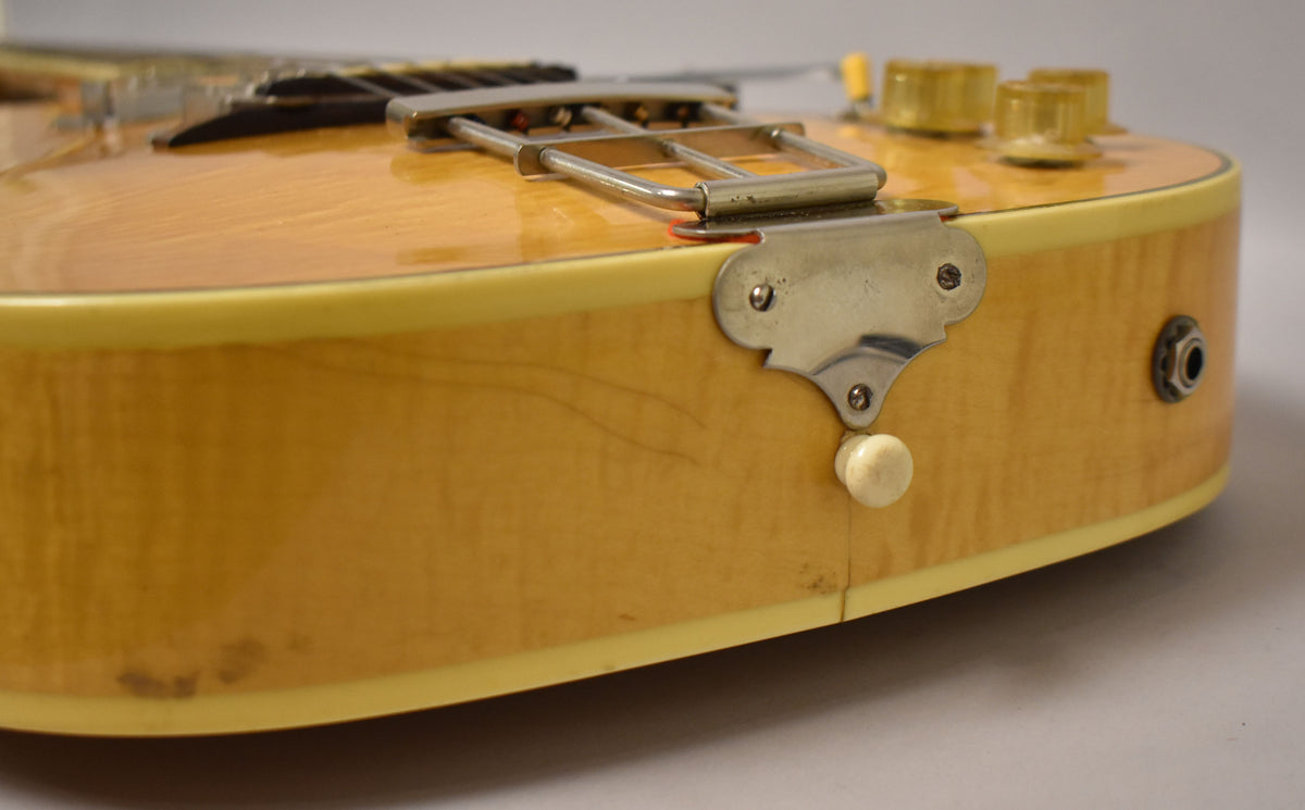 Close-up of the guitar's lower bout, showing the natural finish, chrome trapeze tailpiece, cream binding, and output jack.