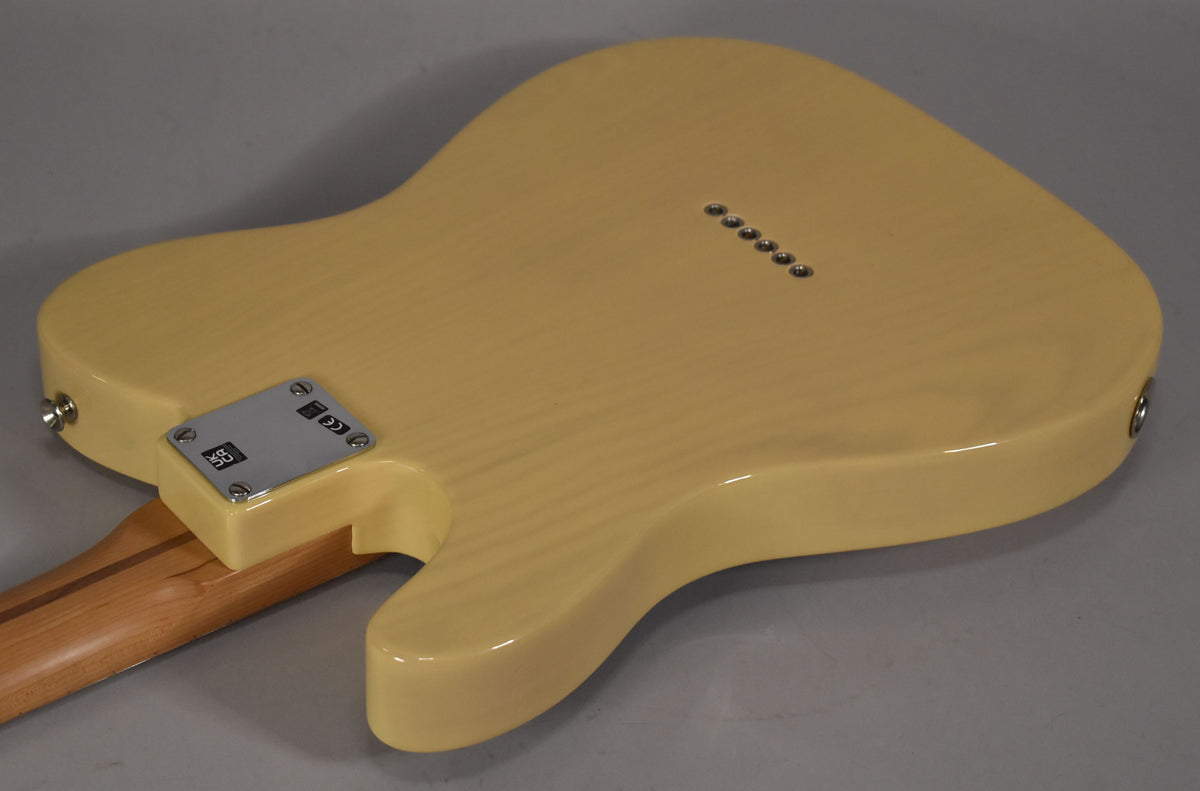 The back of a blonde Telecaster body, showing wood grain through the finish, a chrome neck plate, and six string ferrules.