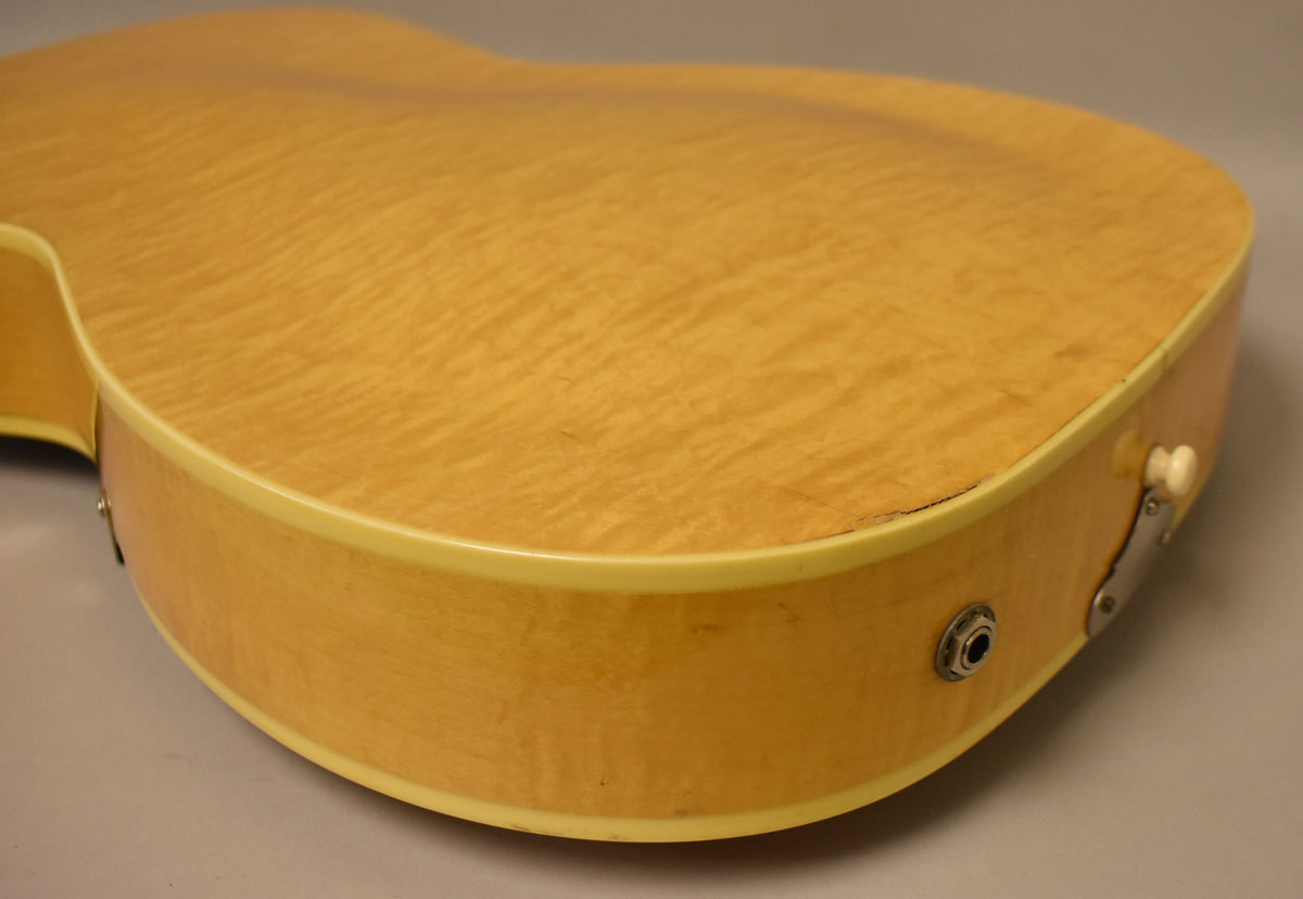 The lower bout of a natural finish archtop guitar, showing the curly maple back, side, output jack, and a crack near the binding.