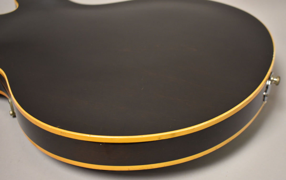 The lower bout of a dark walnut guitar, showing the back and side with cream binding and a strap button.