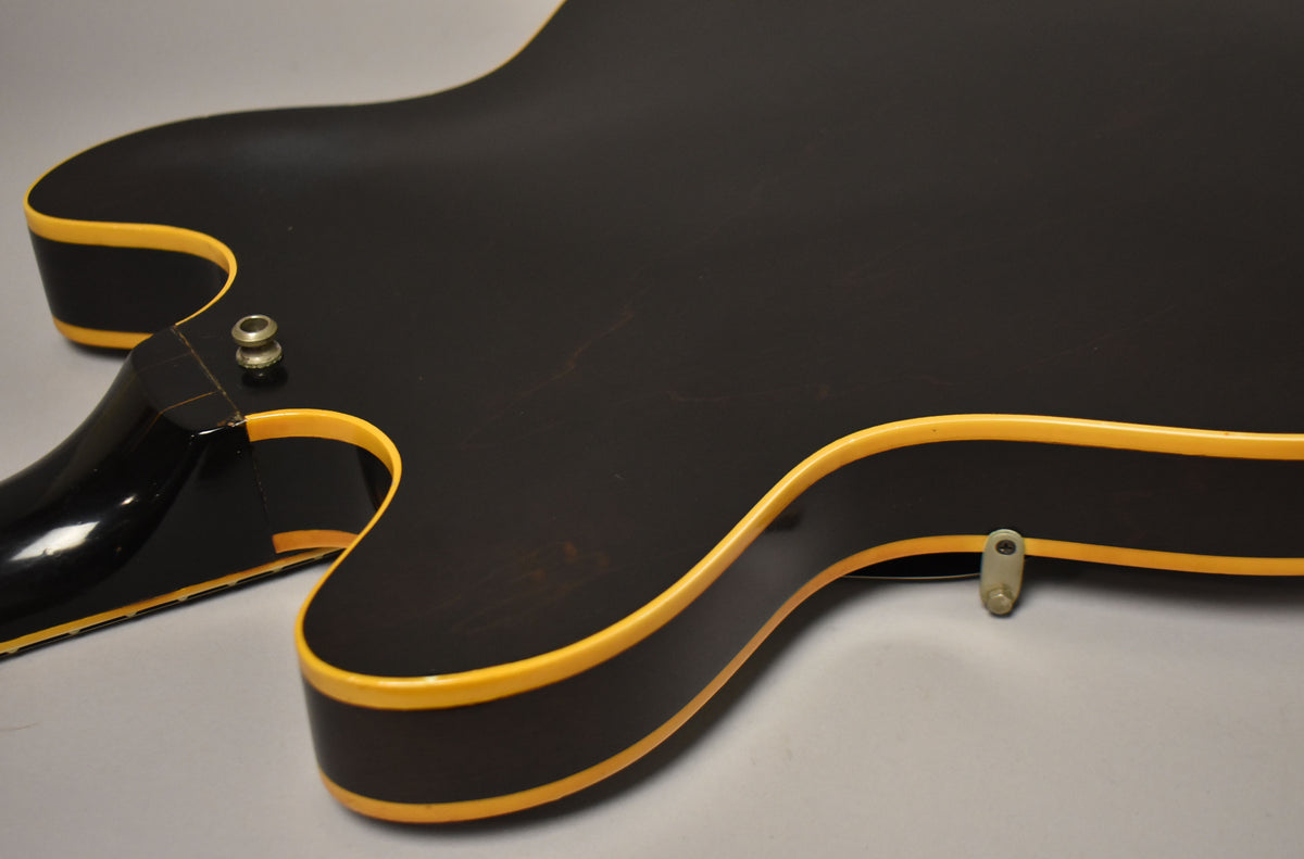 The guitar's lower bout and neck heel are visible from the back, showing a dark walnut finish with yellow binding and light wear.